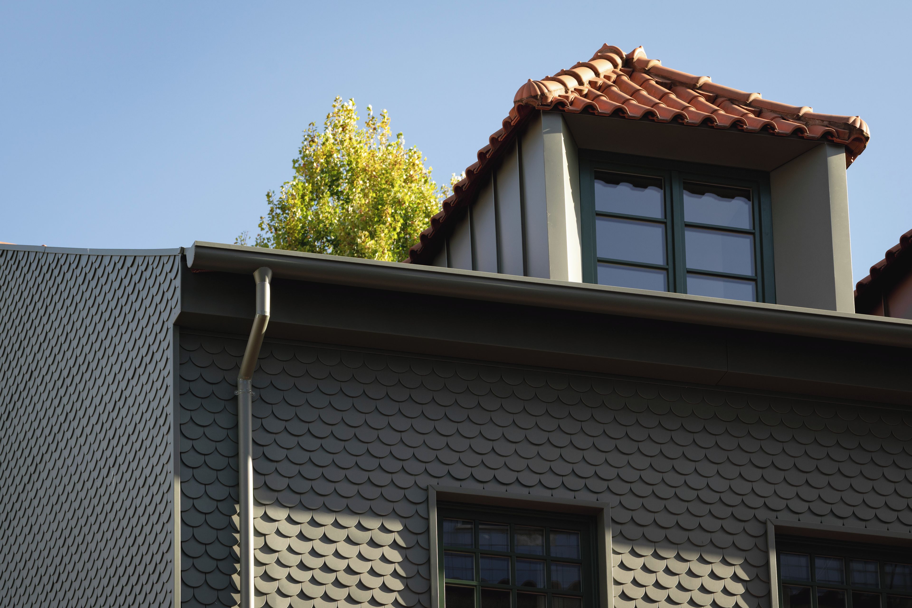 A building with a tiled roof, a window, and a tree.
