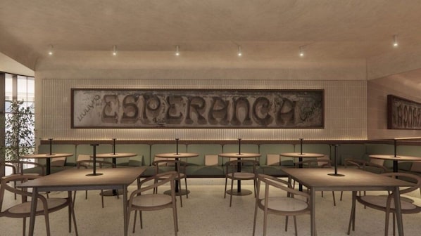 Et restaurantinteriør med flere borde og stole, et stort skilte på væggen med teksten 'ESPERANCE' og en grøn polstret bænk langs væggen.