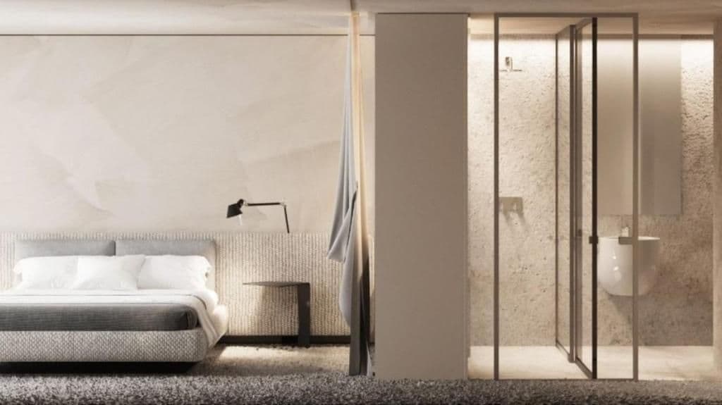 A modern bedroom with a bed, bedside table, and a glass partition separating the room from a bathroom.