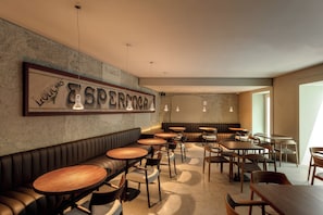 A restaurant interior with a long bench, round tables, and hanging pendant lights.