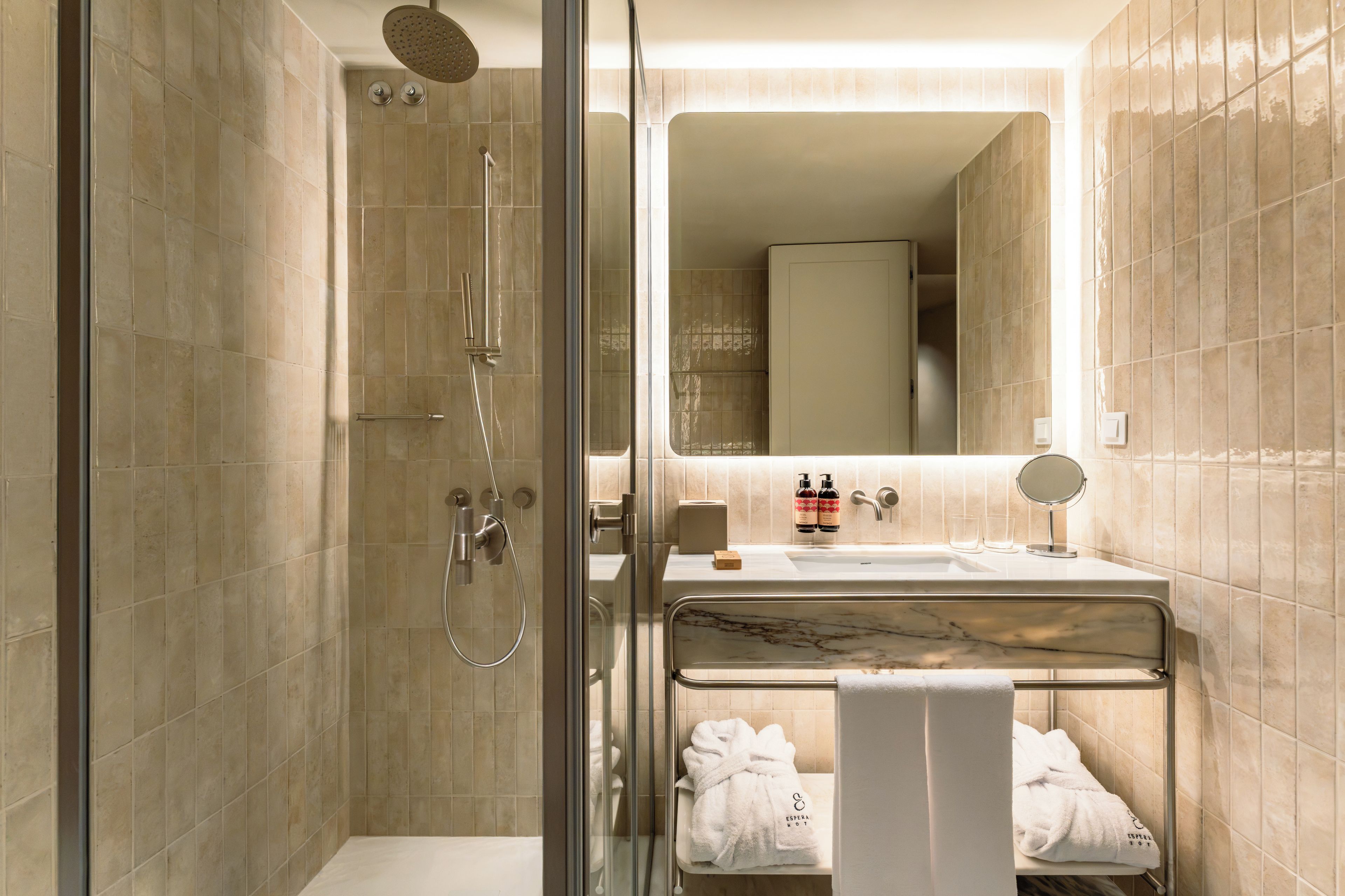 Un baño moderno con ducha envuelta en vidrio, tocador de mármol y espejo.