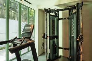 A gym with exercise equipment, including a treadmill and weight machines, with large windows and a view of greenery outside.