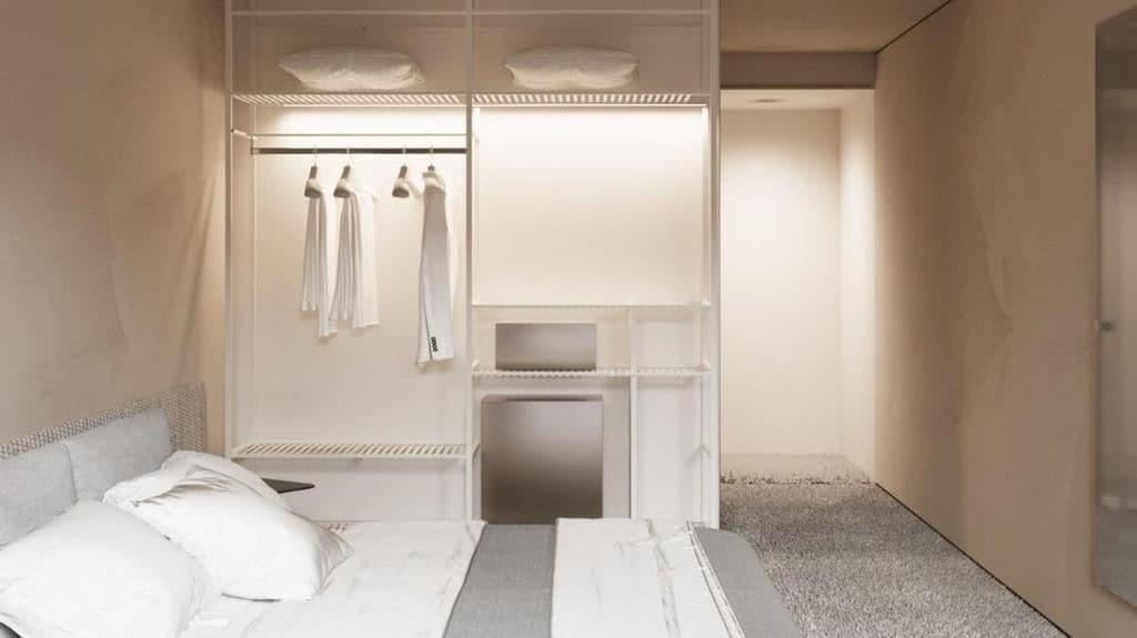 A bedroom with a bed, a built-in wardrobe with hanging clothes, and a bedside table.