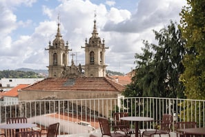 A terrace with outdoor seating, overlooking a historic building with two bell towers and a red-tiled roof. - Esperanca Hotel Braga Vignette Collection By Ihg (Braga)