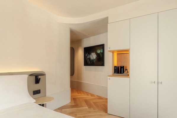 A modern hotel room with a bed, a small table, a wardrobe, and a wall-mounted TV.