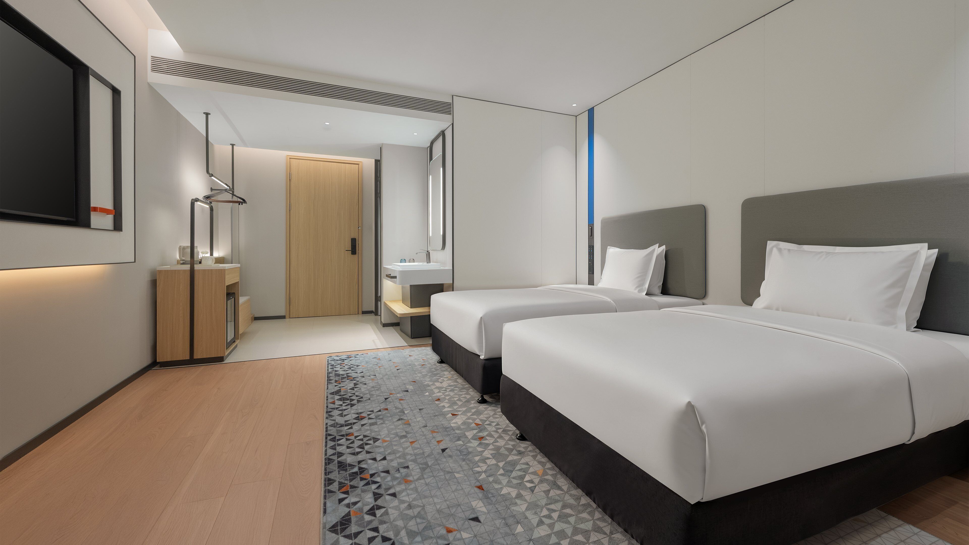 Habitació d'hotel moderna amb dos llits, un mirall gran, un armari de fusta i un bany amb un lavabo i un mirall.