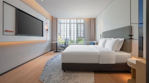 Ein modernes Hotelzimmer mit einem großen Bett, einem Flachbildfernseher, einem Schreibtisch und Blick auf die Stadt.