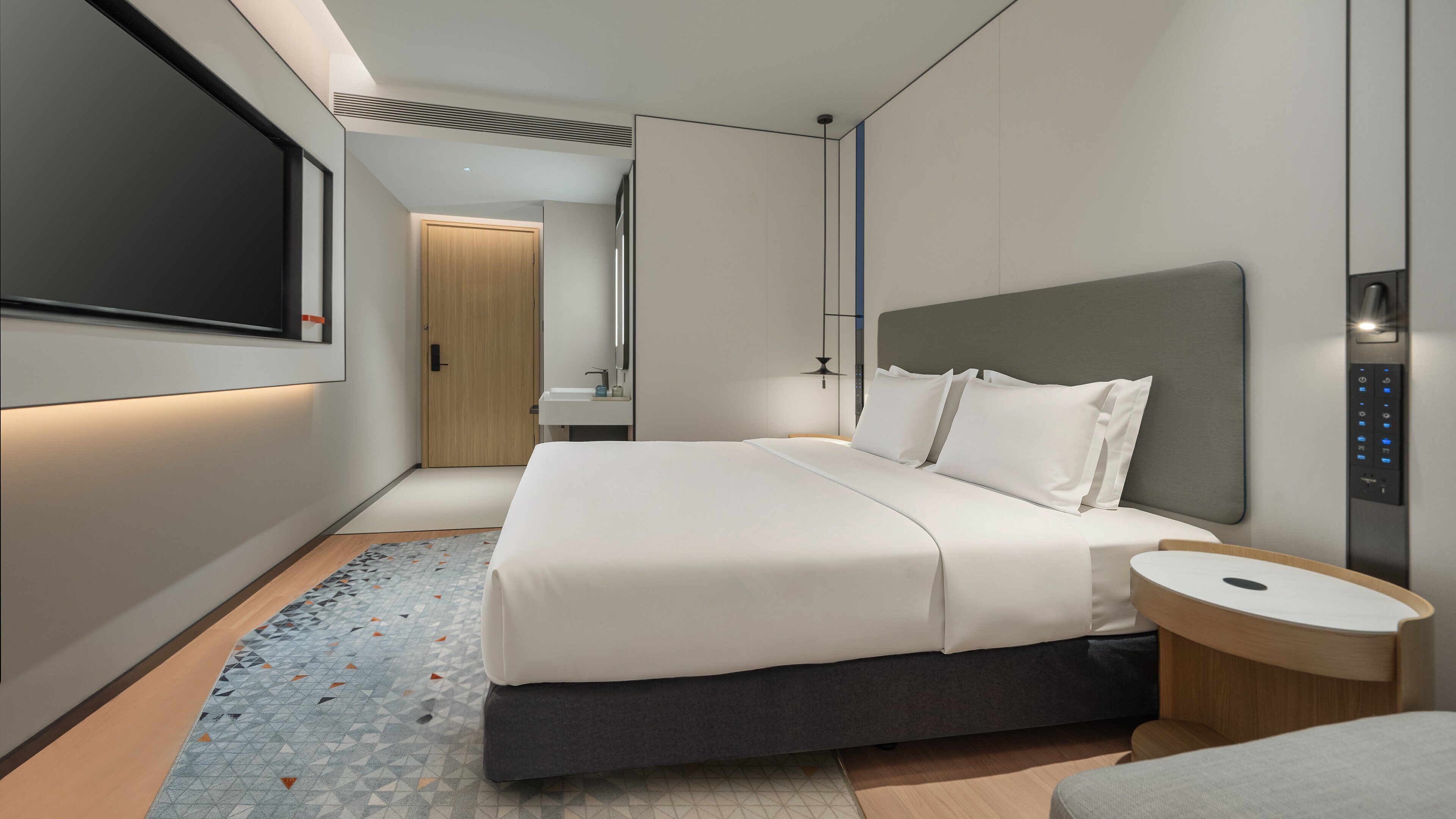 Una habitació d'hotel moderna amb un llit gran, una taula de nit i televisió integrada.
