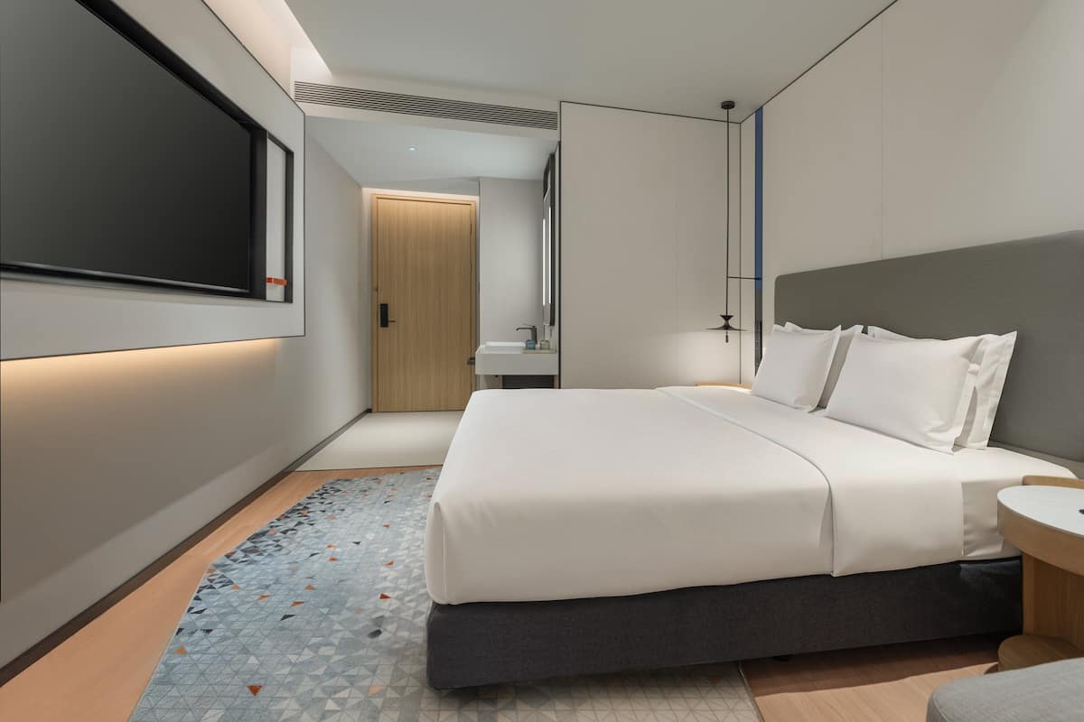 A modern hotel room with a large bed, bedside table, and a built-in TV.