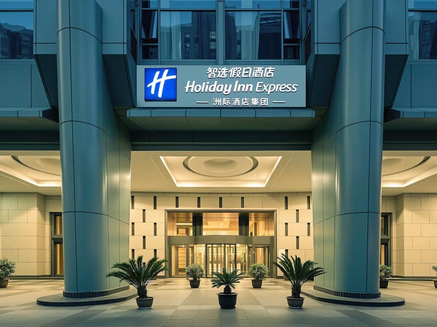 Uma entrada de hotel moderna com a placa Holiday Inn Express, colunas grandes e plantas em vasos.