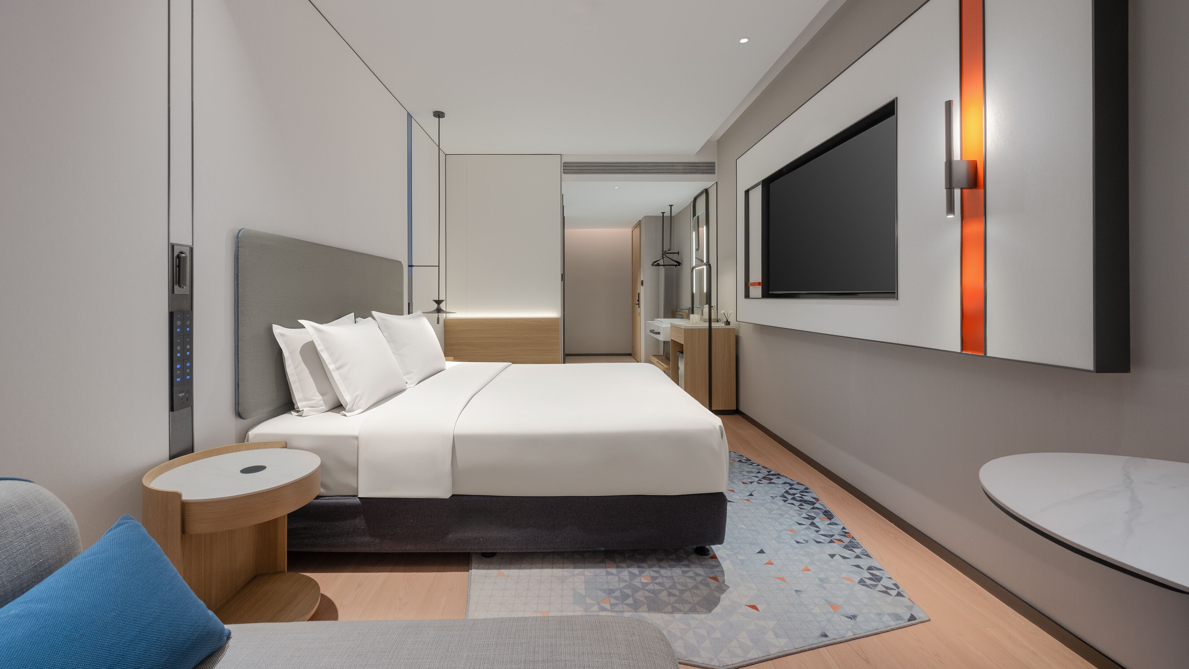 Quarto de hotel moderno com uma cama grande, uma televisão na parede, uma mesa de cabeceira e uma pequena mesa redonda.