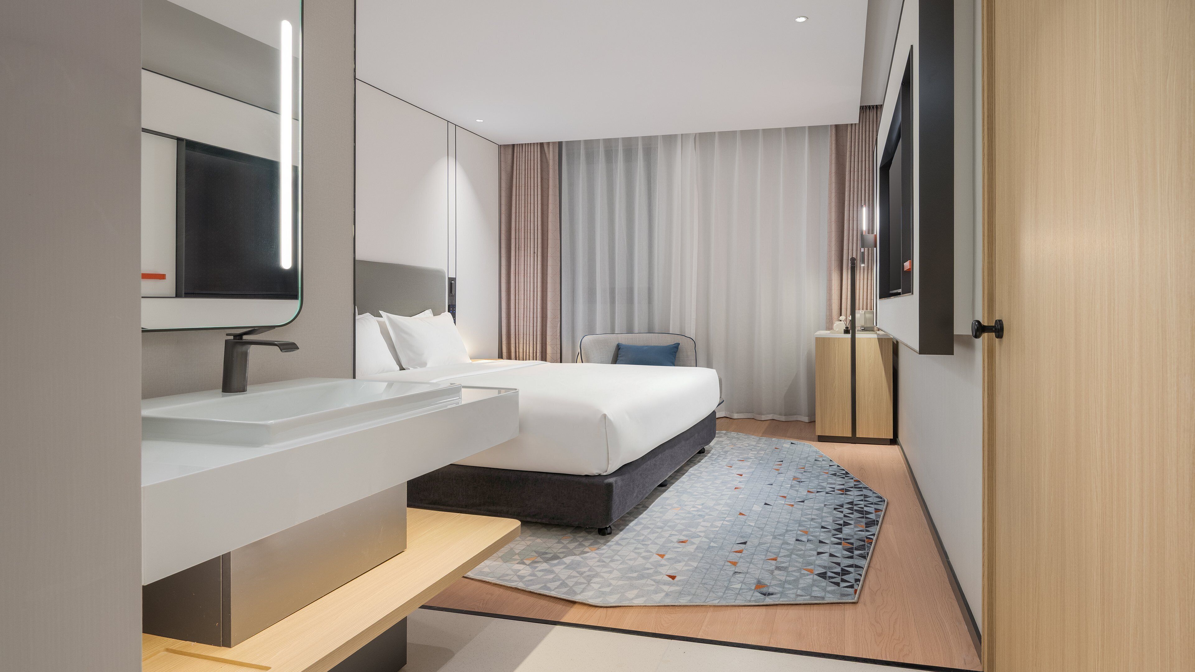 Habitació d'hotel moderna amb un llit gran, una tauleta de nit, televisió integrada i un mirall gran.