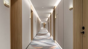 Ein Hotelgang mit Holzwandverkleidung, nummerierten Türen und einem gemusterten Teppich.
