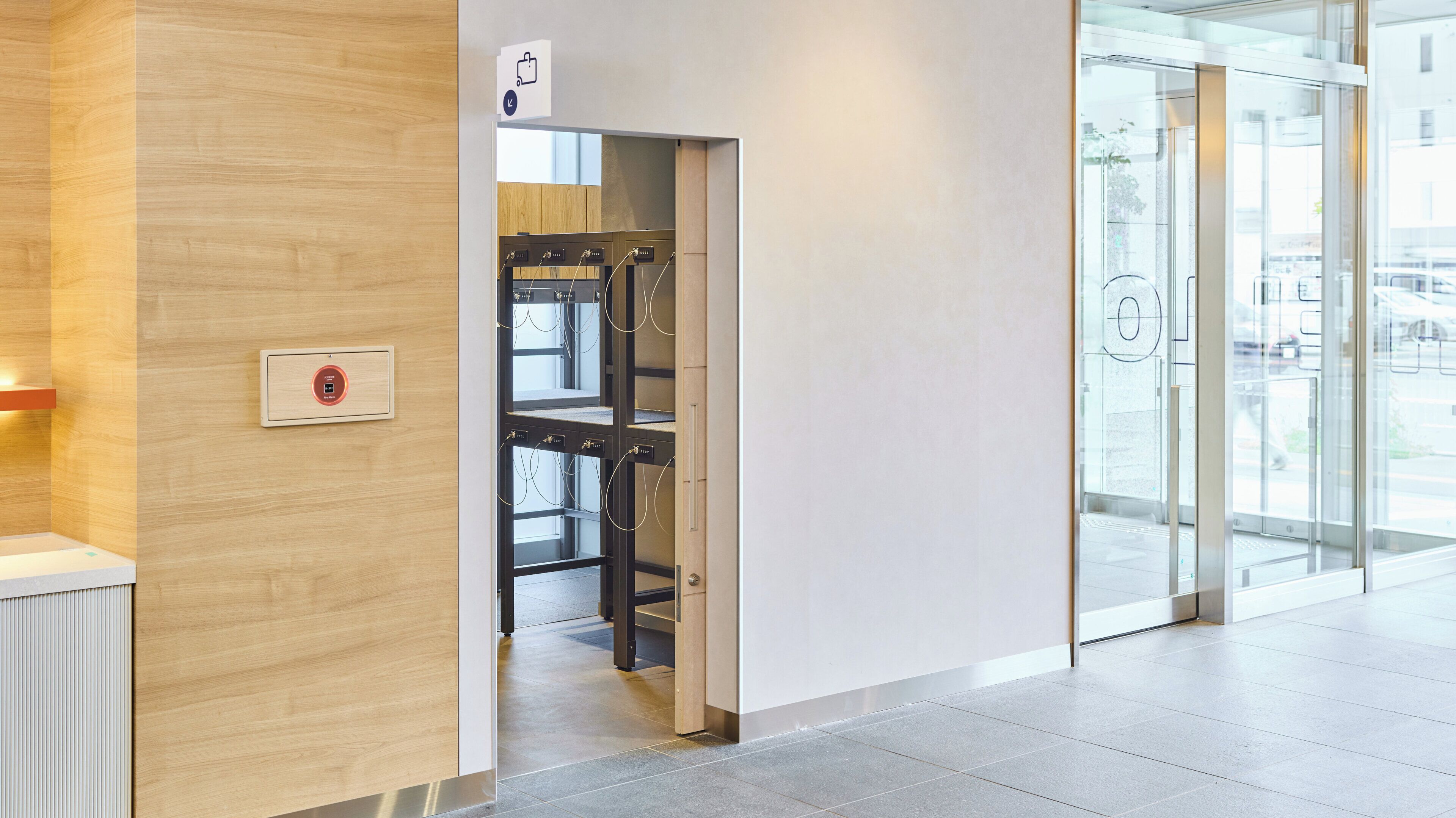 A modern interior with a wooden wall, a glass door leading to a hallway, and a visible fire alarm panel.
