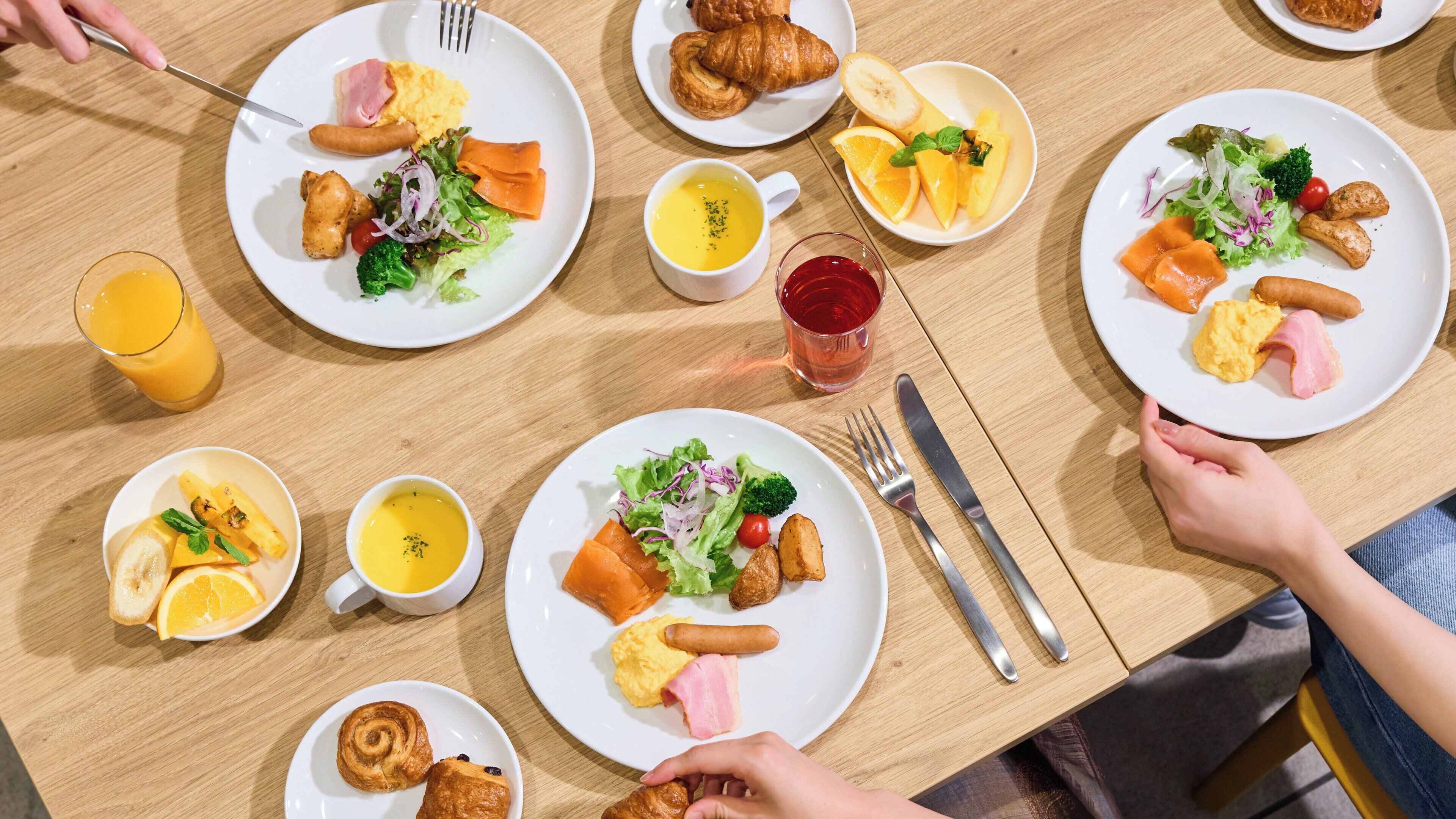 A dining table with multiple plates of food, utensils, and glasses of beverages.