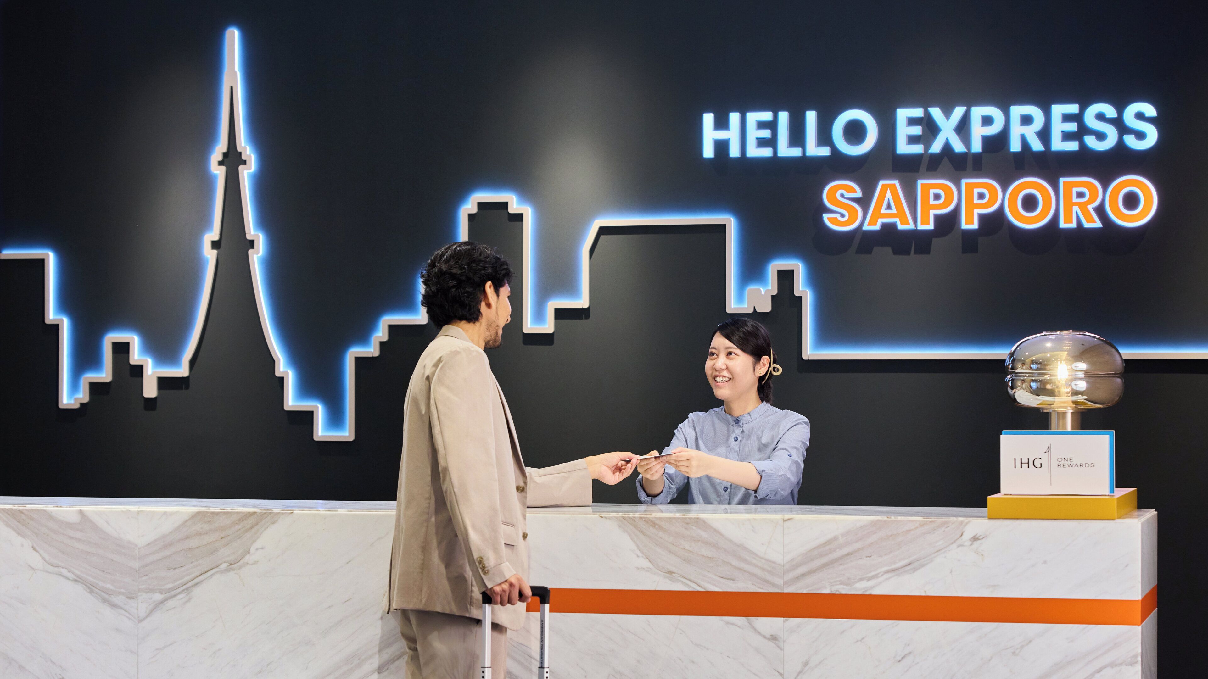 Un comptoir d’accueil avec une enseigne « Hello Express Sapporo », un trophée et un sol en marbre.