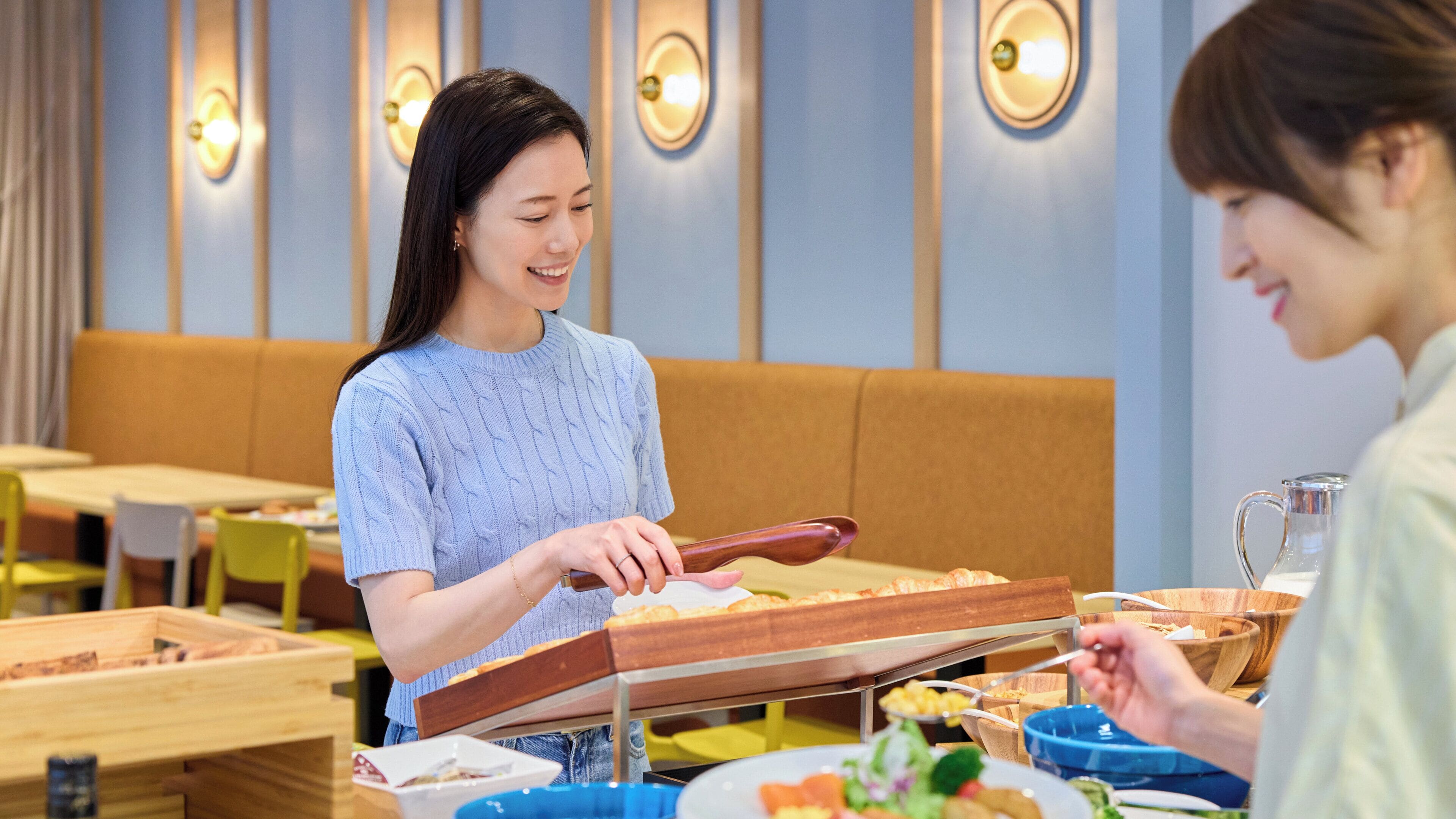 Una persona sirviendo comida en una mesa en un restaurante con diseño interior moderno, que incluye luces montadas en la pared y mobiliario de madera.