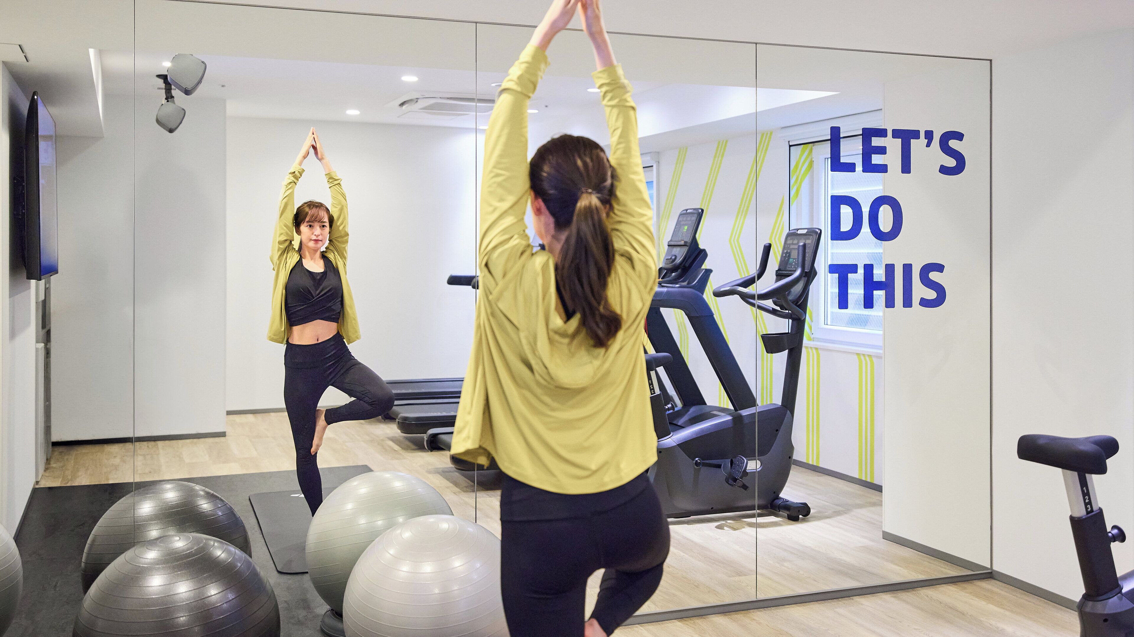 Gimnasio con equipo de ejercicio y un espejo que refleja a alguien estirándose.