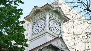 Ein Glockenturm mit zwei Uhren, umgeben von Bäumen und einem Gebäude.