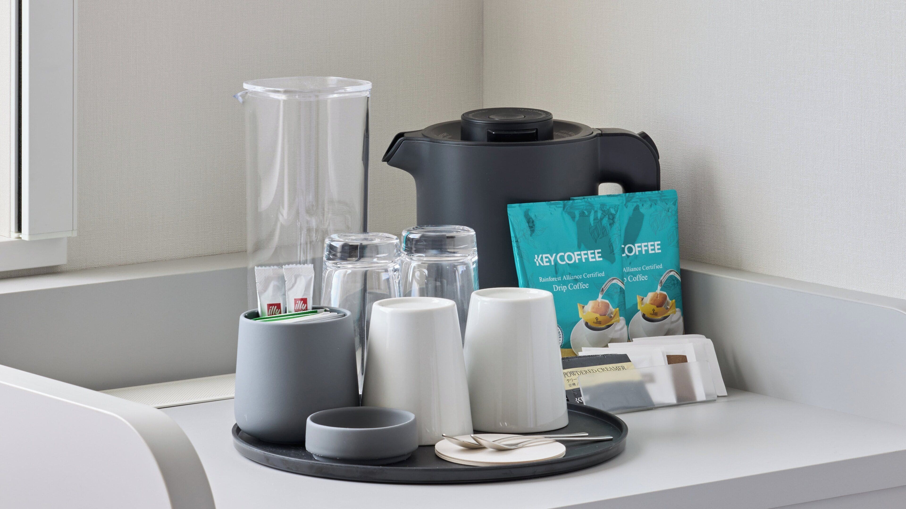 Una cafetera, un dispensador de cápsulas de café, un molinillo de café, una jarra de café y un paquete de café sobre una encimera.
