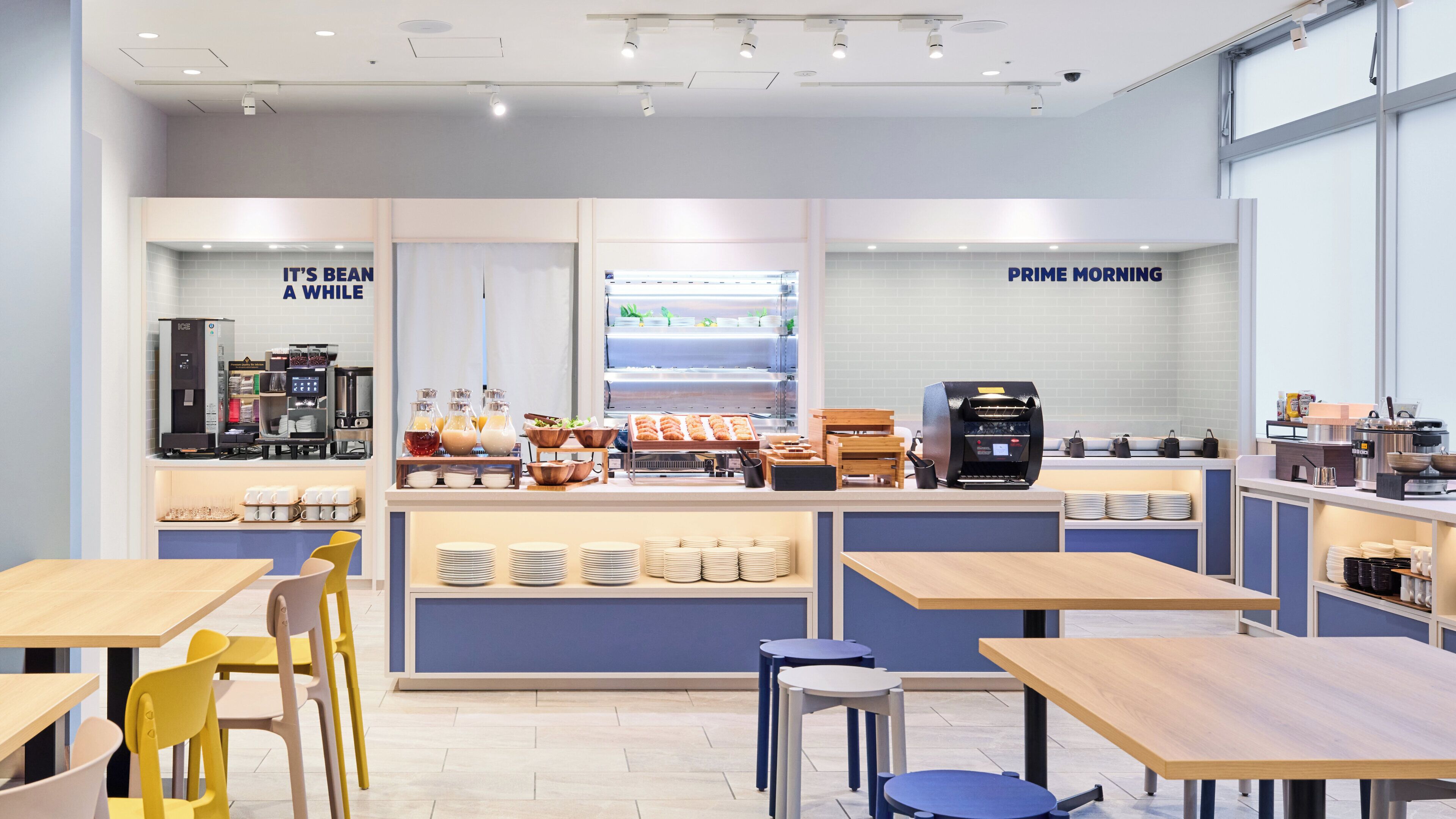 Una cafetería con varias mesas y sillas, una máquina de café y una exhibición de alimentos.