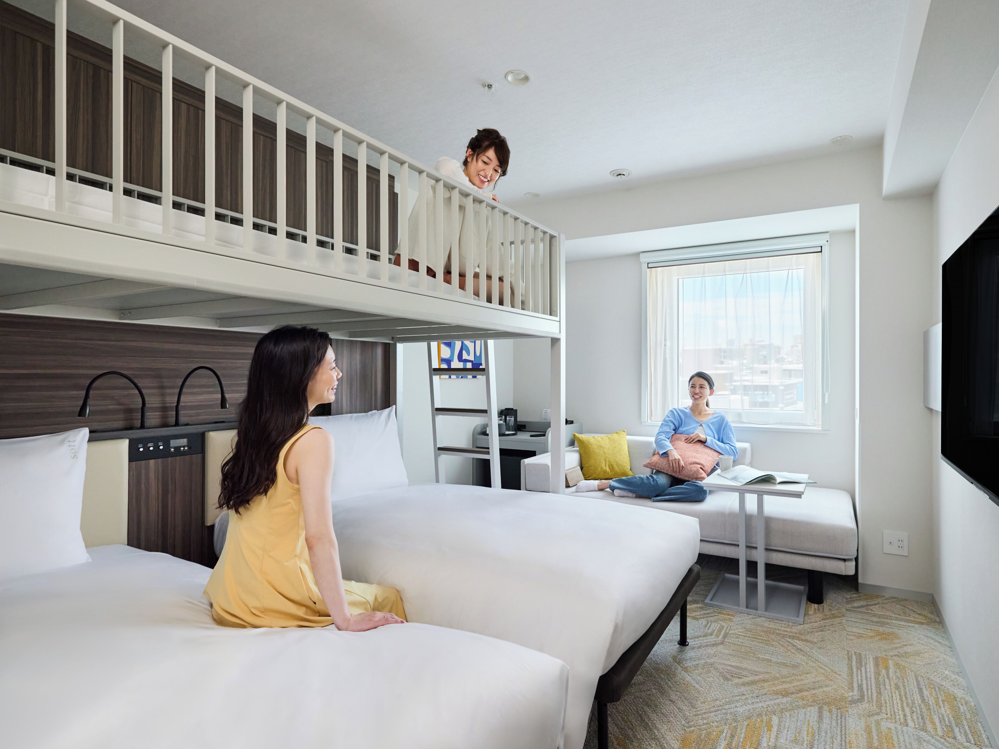 Et hotelværelse med køjeseng, sofa, lille bord og fjernsyn.