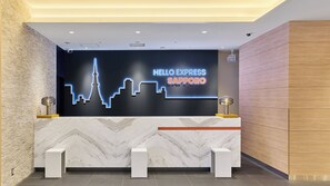 A reception desk with a neon sign reading 'HELLO EXPRESS SAPPORO' and a modern design with marble and wood accents.