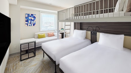 A hotel room with two beds, a sofa, a desk, and a TV.