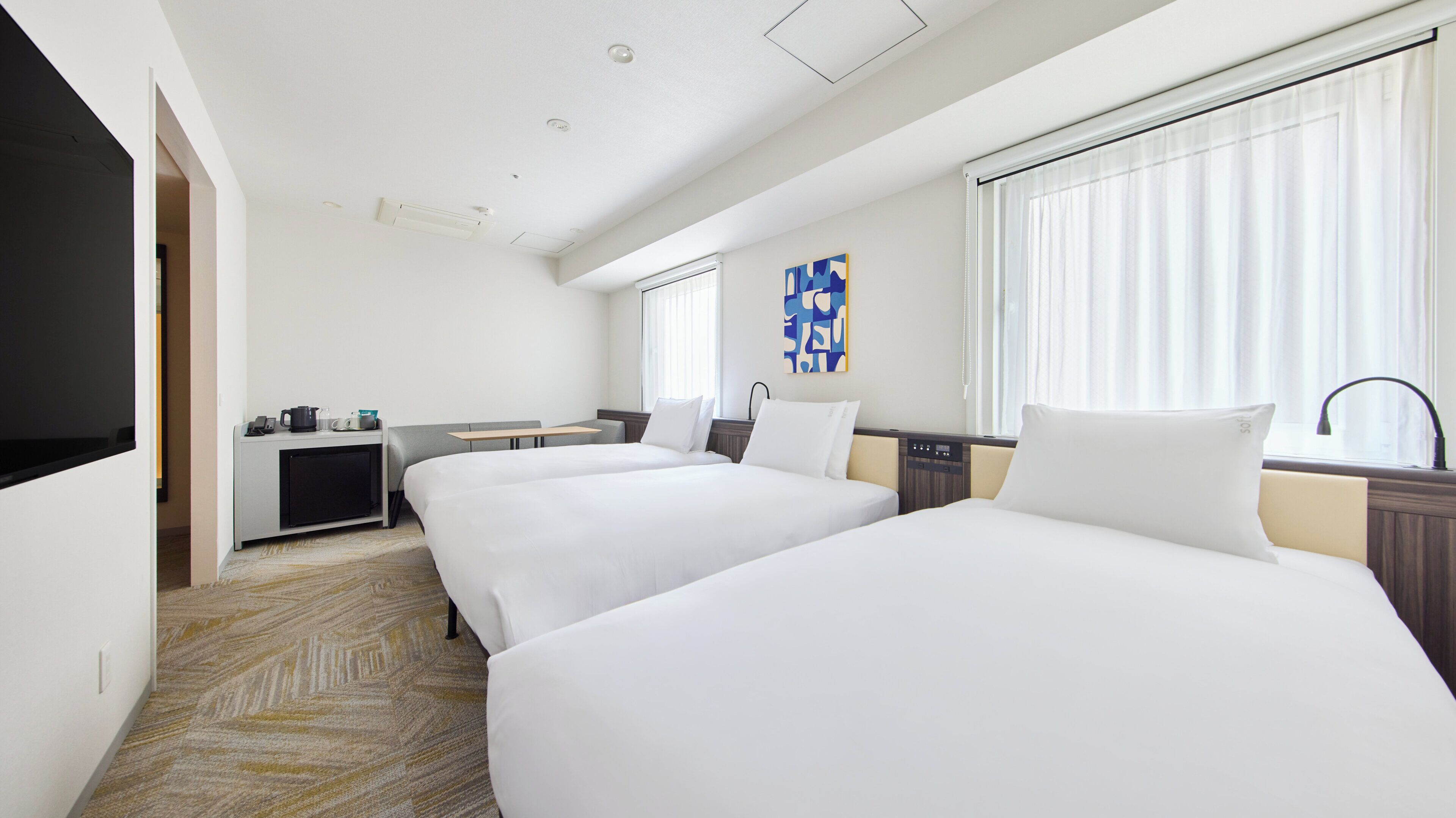 A hotel room with two beds, a desk, a television, and a window with curtains.