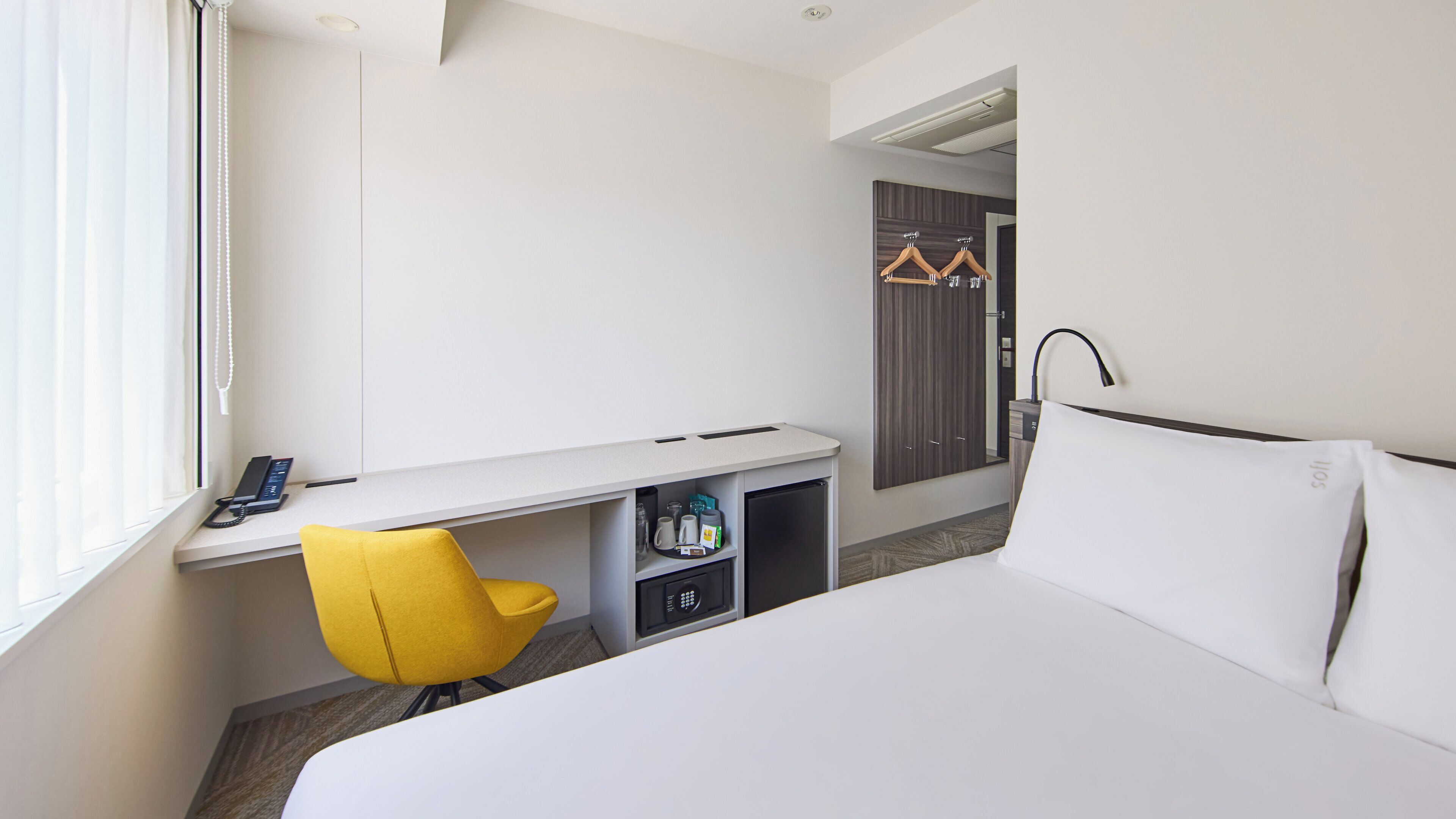 A hotel room with a bed, a desk with a chair, a phone, and a wardrobe.