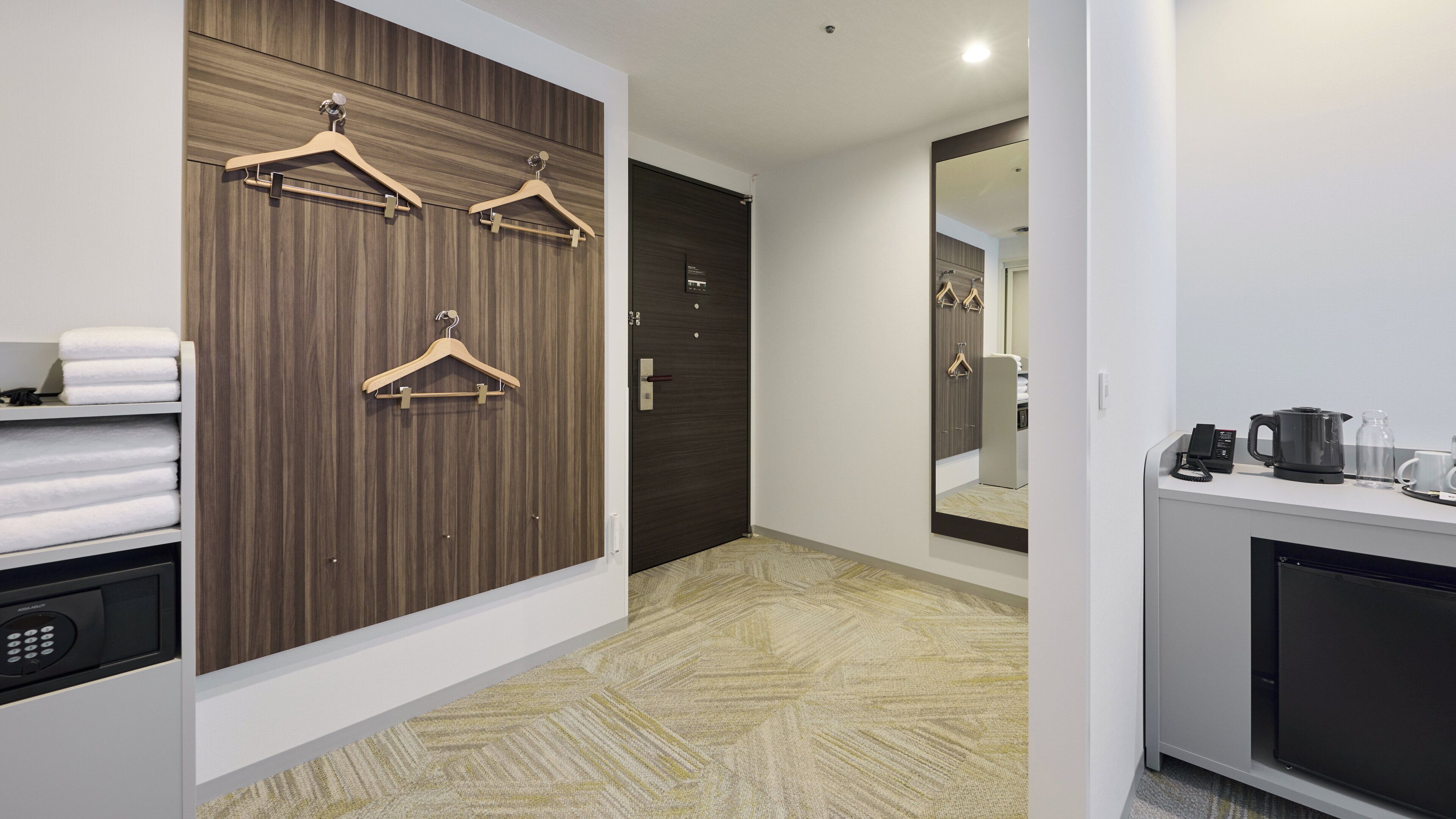 A hotel room with a wooden panel wall, a mirror, a towel rack, a coffee maker, and a small cabinet.