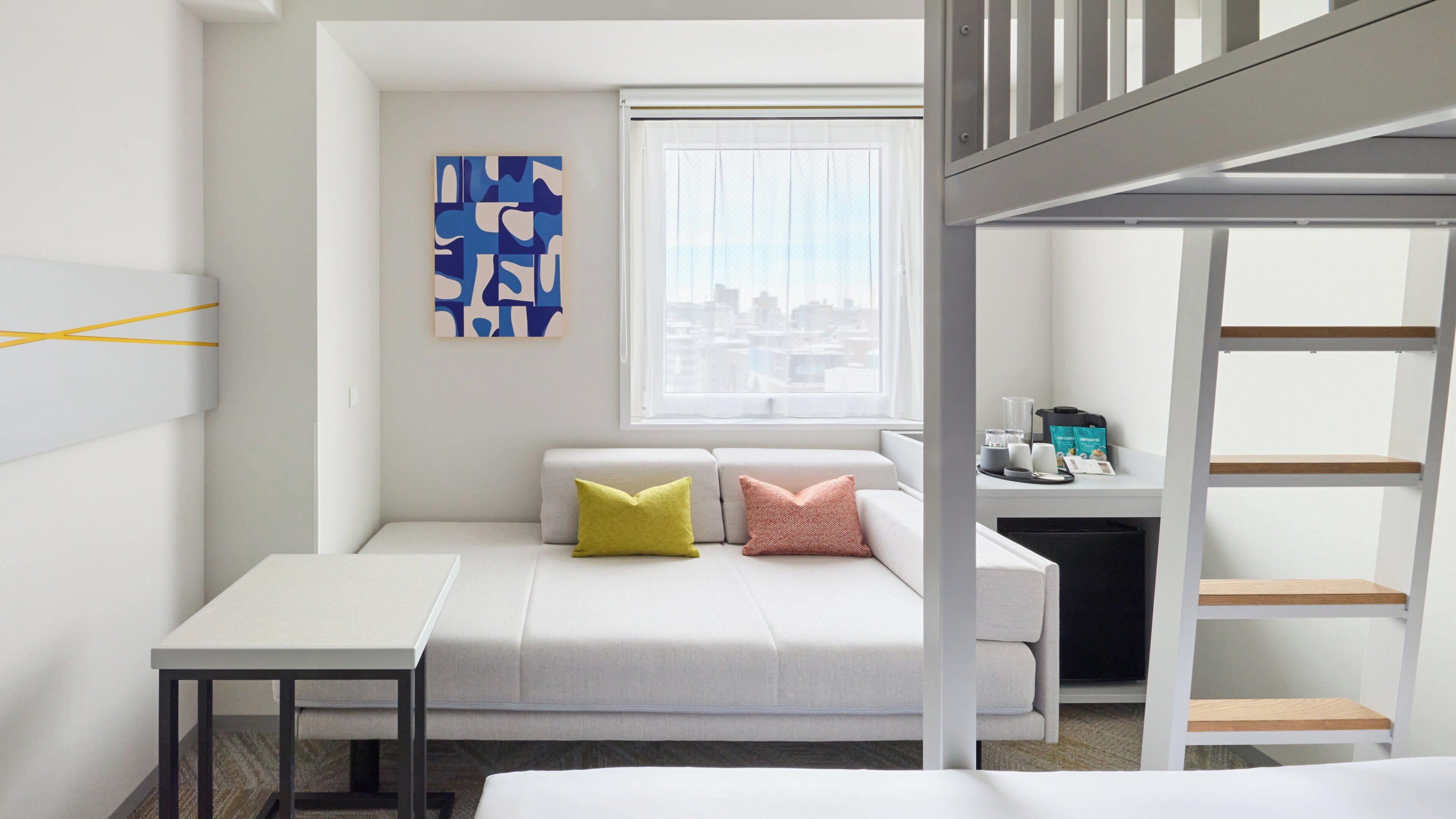 Un dormitorio moderno y funcional con cama, escritorio y ventana con vista a la ciudad.