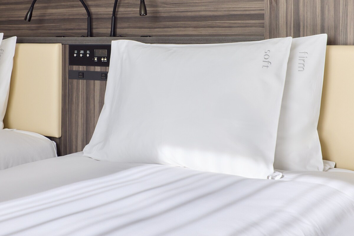 A hotel room with a bed, two pillows, a control panel, and a wooden wall.
