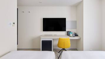Habitación de hotel con cama, escritorio, televisor de pantalla plana, silla y cafetera.