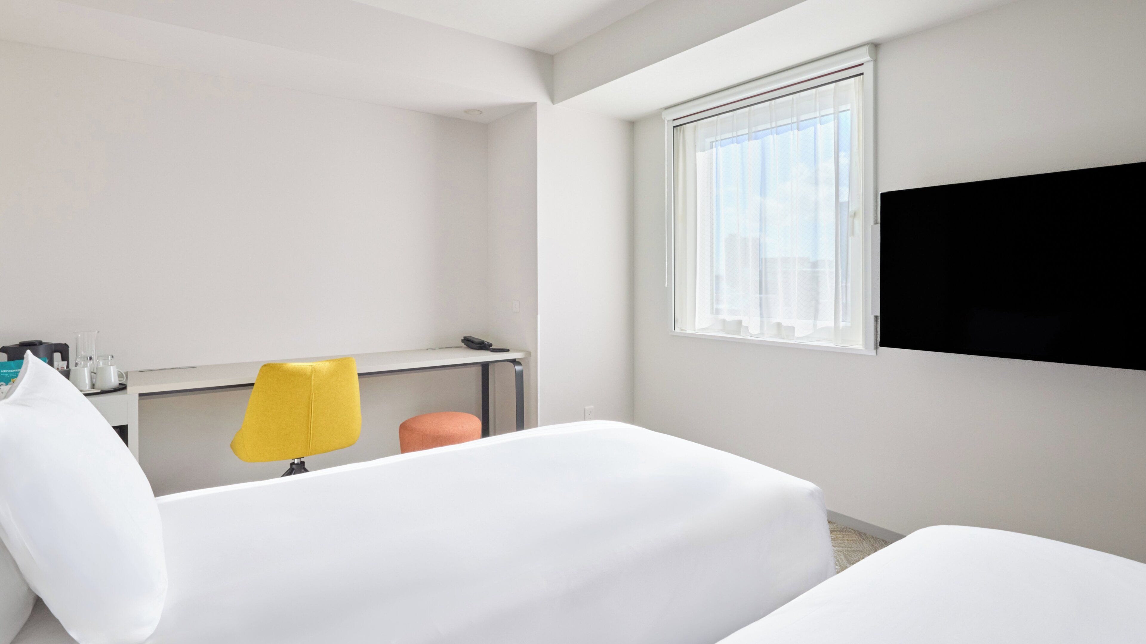 Ein Hotelzimmer mit einem Bett, einem Schreibtisch, einem Stuhl und einem an der Wand befestigten Fernseher.