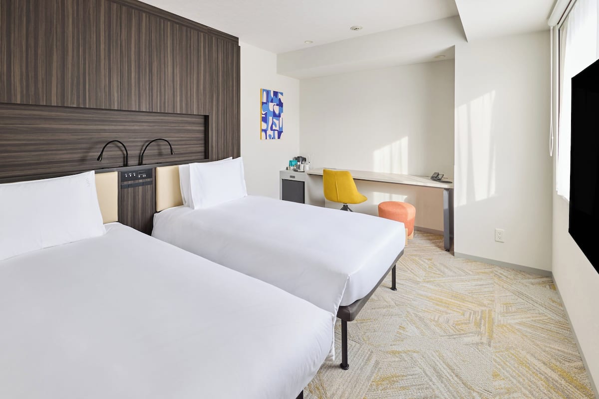 Habitación de hotel con dos camas, un escritorio, una silla y un televisor.