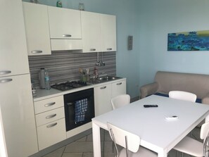Una cocina moderna con armarios blancos, una estufa a gas y un horno empotrado. Hay una mesa de comedor con sillas y un sofá en la sala de estar.