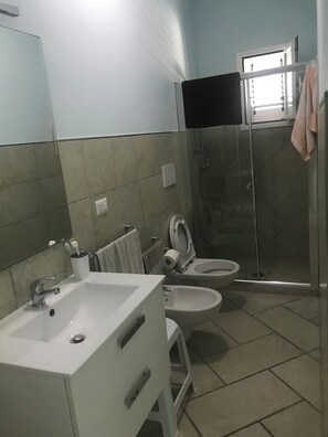 Baño con lavamanos, dos inodoros, ducha y espejo.