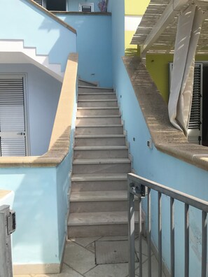 Eine Treppe führt zu einem Hauseingang mit einem Metallgeländer und einer Tür mit einem Fenster.