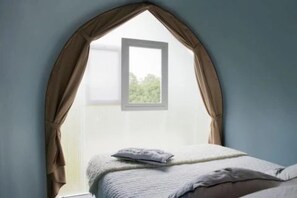 Ein Schlafzimmer mit Bett, einem Fenster mit Vorhängen und Blick auf Grün.