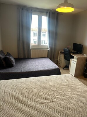 Une chambre à coucher avec un lit, un bureau avec un ordinateur, une chaise et une fenêtre avec des rideaux.