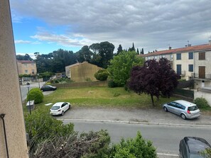 Une rue résidentielle bordée de voitures garées, avec un espace vert et des maisons dotées de balcons.