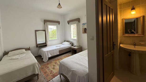 A bedroom with two beds, a window, a mirror, and a bathroom with a sink and mirror. - CİELO HOTEL (Bodrum)