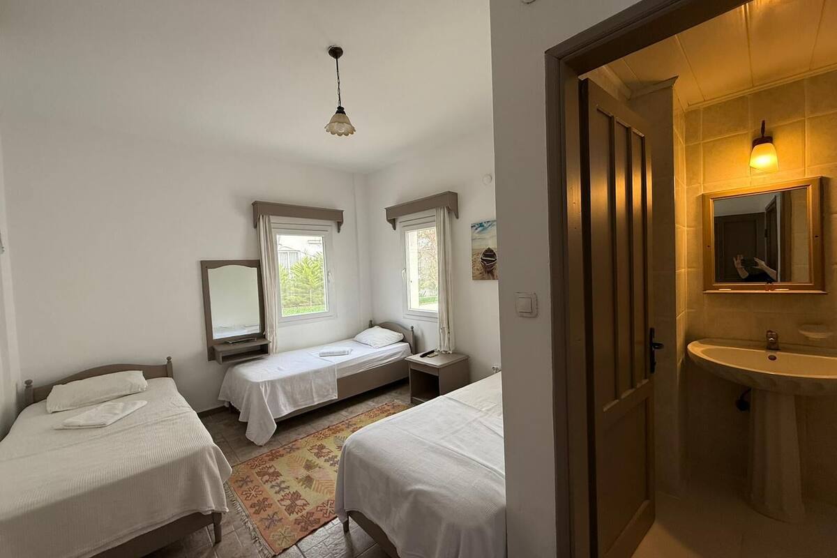 Un dormitorio con dos camas, una ventana, un espejo y un baño con lavamanos y espejo.
