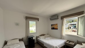 A bedroom with two beds, a window with a view, an air conditioning unit, and a small table. - CİELO HOTEL (Bodrum)