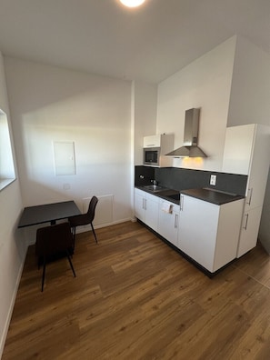 A compact kitchen with a dining table and chairs, a microwave, and a refrigerator.