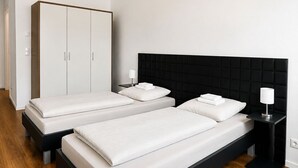 A modern bedroom with two beds, a wardrobe, and a bedside table. - Gauaz Boardinghouse  (Maisach)