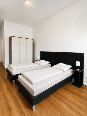 Un dormitorio moderno con dos camas, un armario y una mesita de noche.