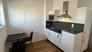 A compact kitchen with a microwave, stove, and cabinets, a small dining table with chairs, and a window. - Gauaz Boardinghouse  (Maisach)