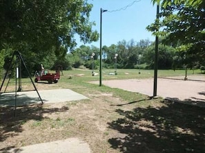 Ein Park mit einer Schaukel, einem roten Fahrzeug und einem befestigten Bereich.
